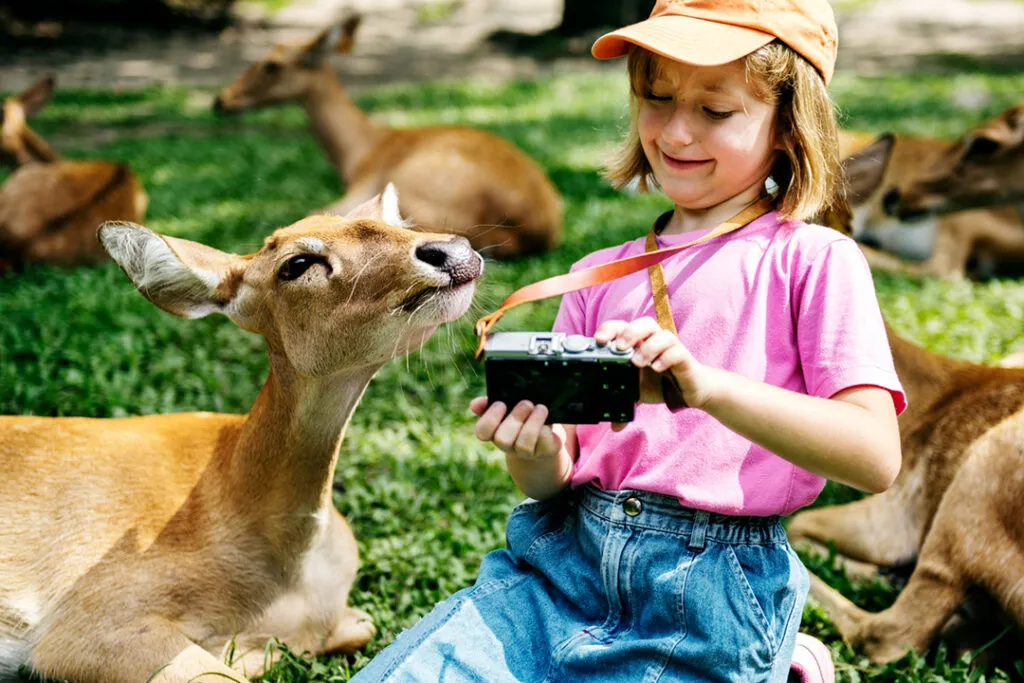A young girls takes a photo with a female deer.
